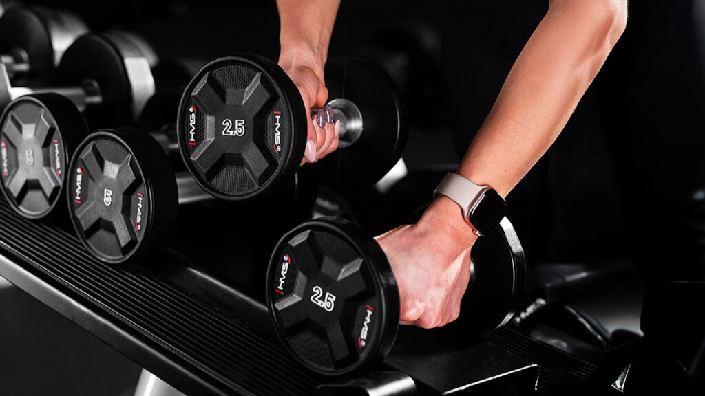 3. Detail rukou uchopujících lehké jednoruční činky na stojanu v posilovně